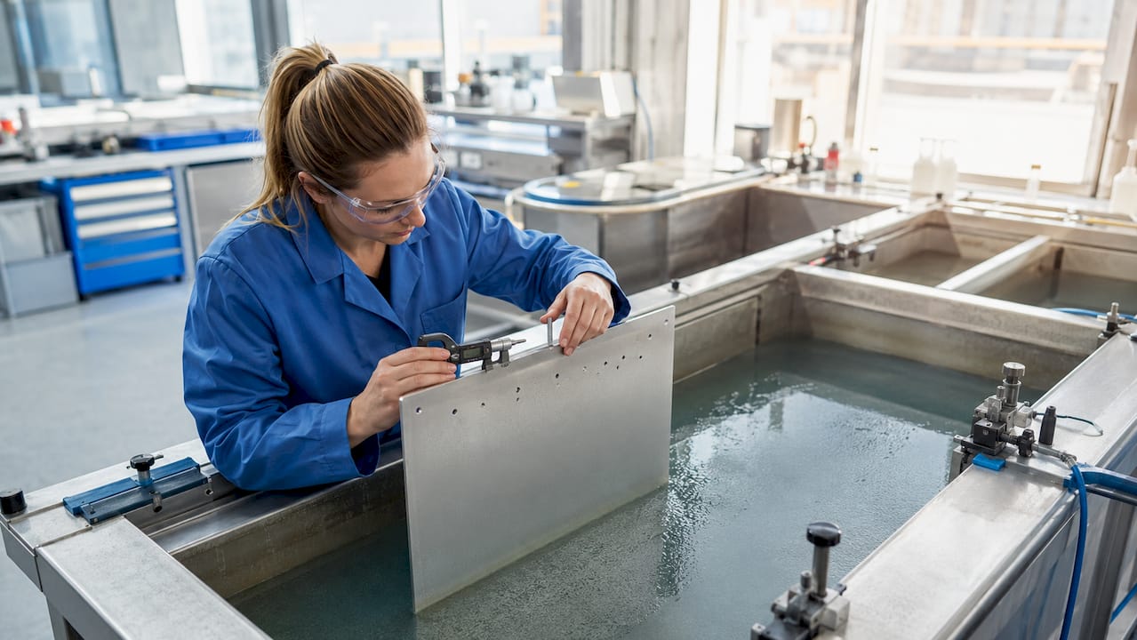 Een technicus controleert een geanodiseerde aluminium plaat op kwaliteit.