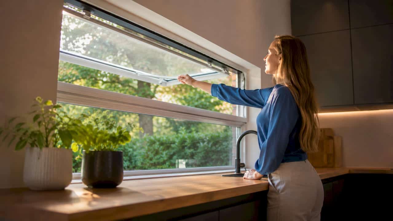 In een lichte badkamer zet een vrouw het raam op een kier.