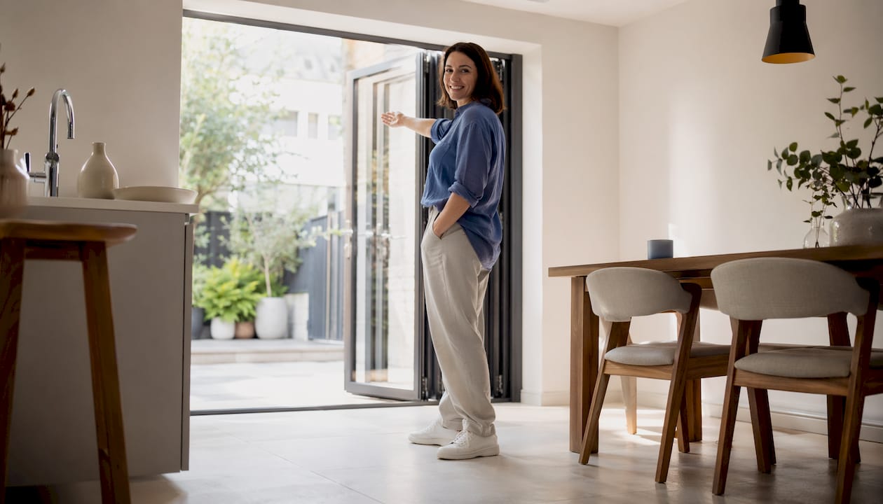 Een vrouw schuift de aluminium vouwwanden open om de woonkamer te verbinden met de tuin.