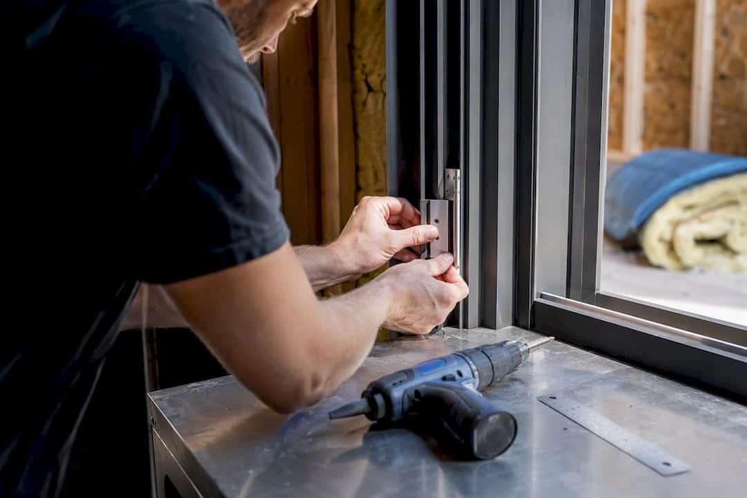 Een paar handen monteert een aluminium scharnier op een raam.