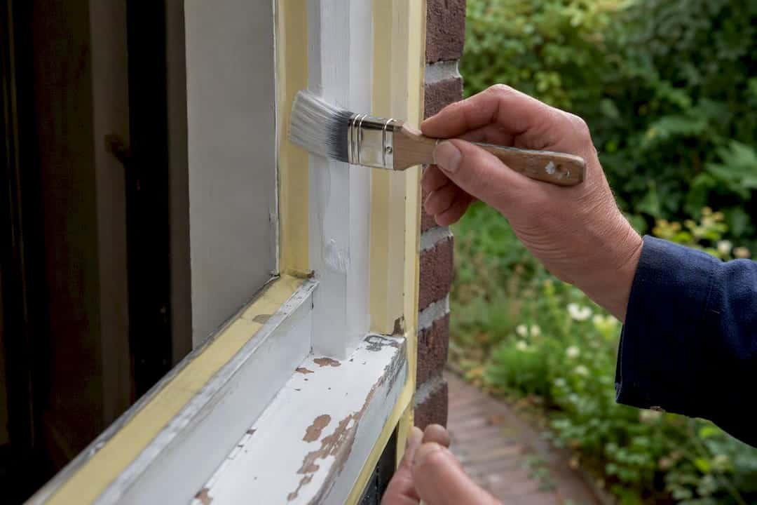Handen die een gerenoveerd deurkozijn schilderen
