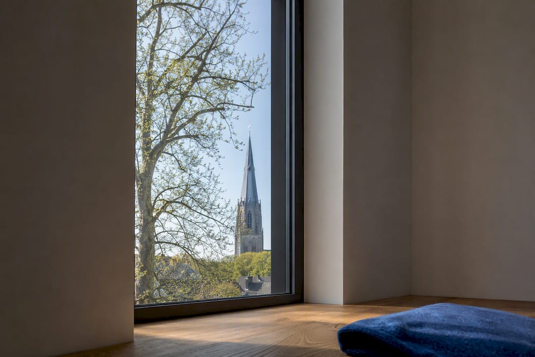 Smalle raamopening omlijst boom en kerktoren