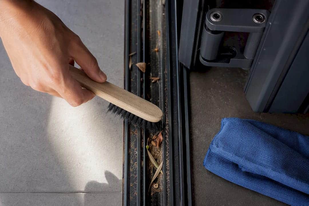 Hand die de vloerrail van een vouwpui schoonmaakt