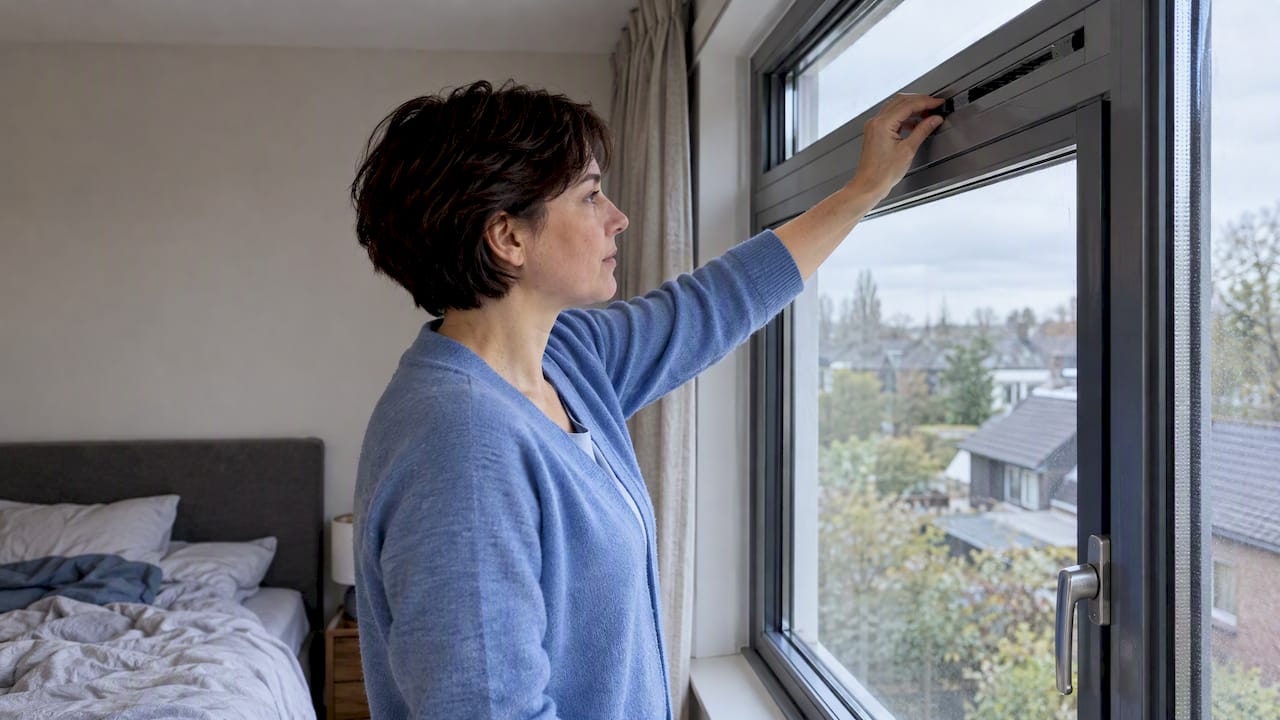 Bewoner opent het ventilatierooster boven het aluminium raam